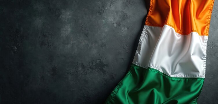 Irish tricolor flag lies on dark background. National symbol of Ireland with orange white green colors. Irish identity, culture, tradition, heritage, celebration, patriotism is expressed with banner.