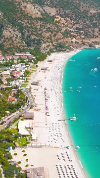 Vertical video. Oludeniz, Turkey. Aerial drone view from above of a yellow parasail over a speedboat on turquoise sea, Oludeniz Beach and mountain coastline in background, summer.. Aerial View. Rich 