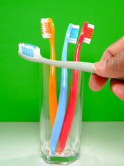 A set of colorful toothbrushes in a clear glass on green background with one of hand holding, conveying a sense of oral hygiene and daily routine with a touch of vibrancy.