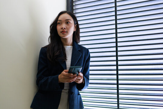 Professional woman holding smartphone contemplating by window - Powered by Adobe