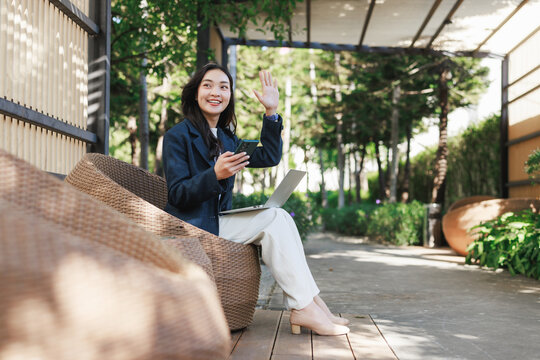 Young asian woman waving hello, remote working outdoors
