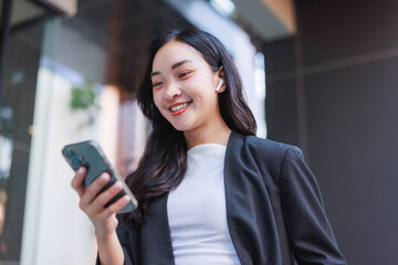 Young asian woman smiling, enjoying smartphone and wireless earbuds