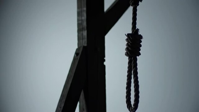 A gallows with a noose, silhouette against a gray sky