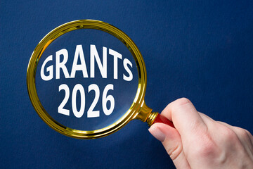 Grants 2026 symbol. Magnifying Glass with words Grants 2026. Businessman hand. Beautiful deep blue background. Business and Grants 2026 concept. Copy space.