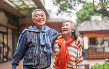 Naklejka premium Happy senior asian couple walking and laughing together outdoors, elderly husband and wife enjoying retirement lifestyle and travel in winter, active aging, insurance and health care concept