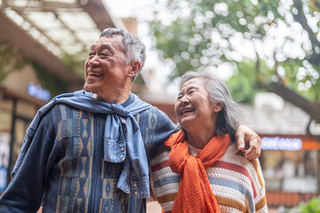 Naklejka premium Happy senior asian couple walking and laughing together outdoors, elderly husband and wife enjoying retirement lifestyle and travel in winter, active aging, insurance and health care concept