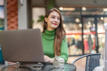 Happy woman freelancer digital nomad working online on laptop, content creator marketer planning social media strategy waiting for travel transport, workation and remote work at cafe coffee shop