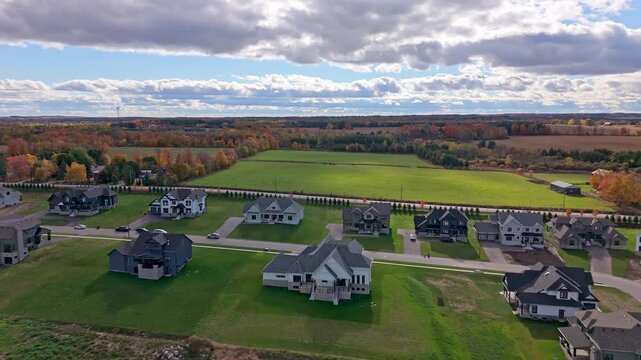 Drone glides over a new subdivision in Alton, Caledon, Ontario with detached houses, green lawns, and farmland beyond under dramatic autumn clouds.