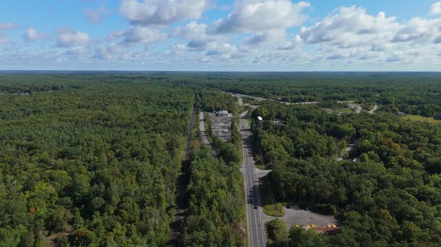 Drone view of a straight rural road cutting through dense green forest near Gravenhurst, Muskoka, Ontario, Canada under scattered clouds.