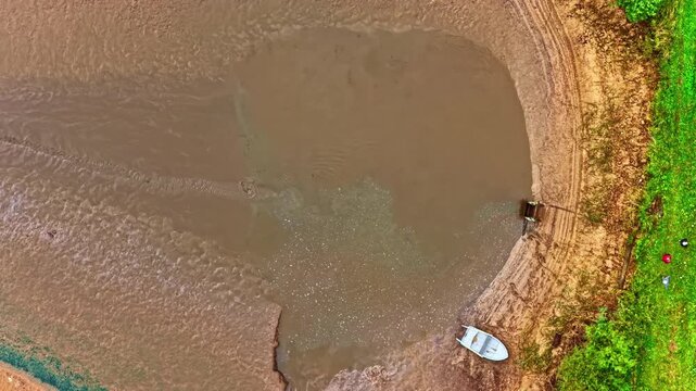 Aerial timelapse of a pond draining into a narrow outlet, revealing shifting mud patterns, exposed basin edges, and rapid water recession.