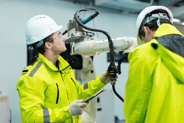 Engineer inspecting industrial robotic arm in smart factory, highlighting automation technology, robotics maintenance, safety protocols and teamwork in modern manufacturing environments.