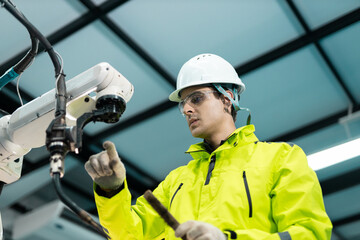 Engineer inspecting industrial robotic arm in smart factory, highlighting automation technology, robotics maintenance, safety protocols and teamwork in modern manufacturing environments.