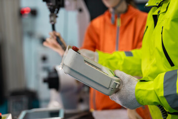 Close-up of engineer operating industrial robotic arm using handheld controller, illustrating robotics programming, automation control and teamwork in smart factory environments..