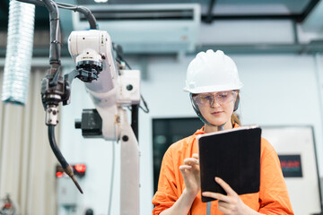 Female engineer using tablet to control robotic arm in smart factory, showcasing automation, industry 4.0, advanced manufacturing technology for efficient production management.