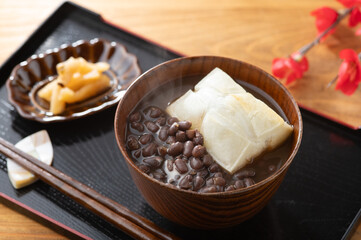 木製のテーブルに置かれた和風のお盆にある湯気の立つぜんざいと漬物