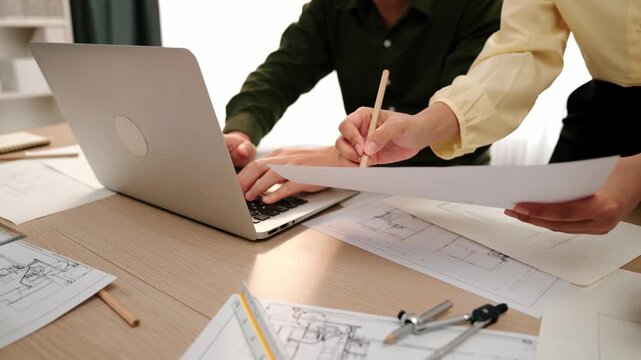 Architect and engineer compare construction detail blueprint display in laptop on table with architectural document or plan and measurement tool for accuracy at modern office. Closeup. Delineation.