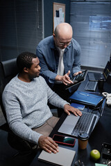 Middle aged Caucasian man showing information on digital tablet to young adult Black man sitting at...