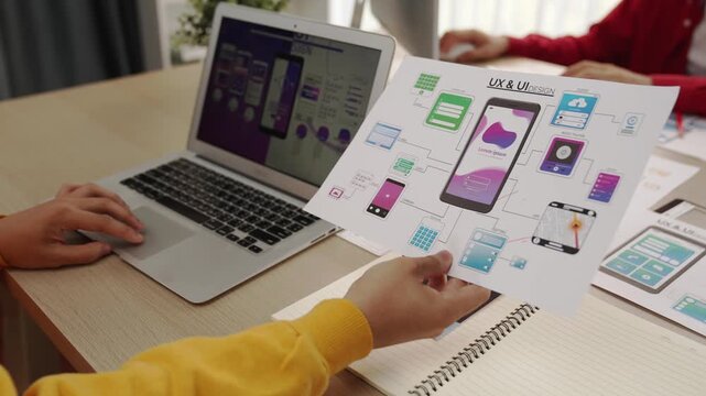 Excellent startup company employee presenting user interface prototype for mobile application to smart co-worker in office workspace. UX UI designer explain function of icon design on paper. Synergic