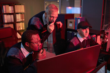 Middle aged Black man, Caucasian man, and middle aged man monitoring security footage on computer...