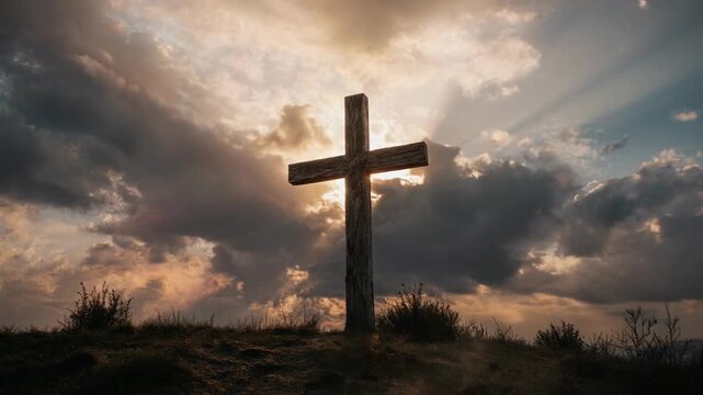 A large, weathered cross standing on a hill with the sun shining through it, surrounded by cloudy skies and patches of grass