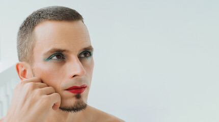 adult gay man with makeup and cosmetics on his face. A handsome transgender male with red lipstick on lips and mascara on eyes on a white background