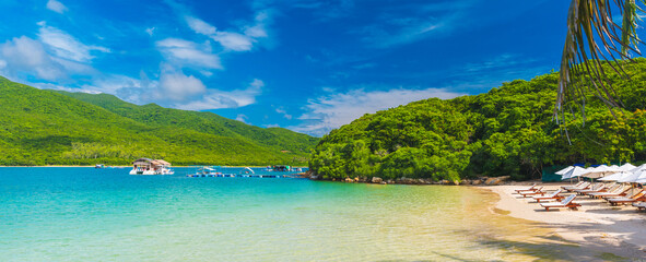 landscape panorama with sandy beach with sun loungers and umbrellas in blue lagoon by sea on sunny summer day at resort on a paradise island
