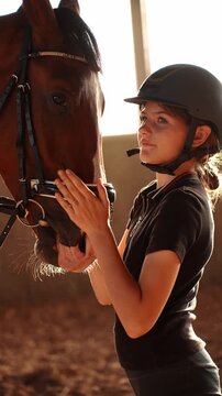 Girl carefully adjusts horse's harness, showing care for it by touching it. Rider carefully places bridle on horse in arena in daylight. Girl carefully prepares horse for riding. Riding, love and care