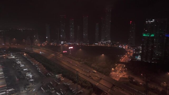 Night drone view over Gardiner Expressway near Parklawn, Etobicoke, Toronto, with condo towers and Ontario Food Terminal yards lit by streetlights and moving traffic.