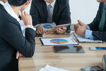 Group of business people meeting to analyze financial data charts on table. Close up team hands working with digital tablet and smartphone during marketing strategy conference.