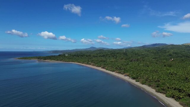 Aerial drone footage of a remote sandy beach on Tablas Island near Odiongan, Philippines, featuring dense green palm forest and rolling mountains in the background on a bright sunny day.