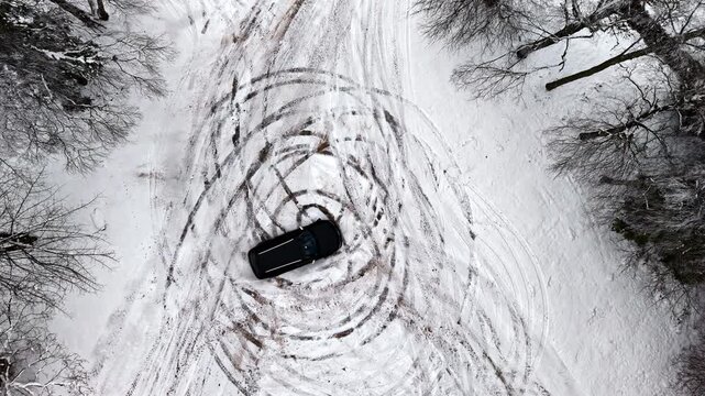 Top view of a black car doing donuts in the snow.