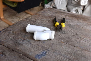 White PVC S-type drainage gully trap pipe fittings and yellow-handled diagonal cutting pliers on a rustic wooden table
