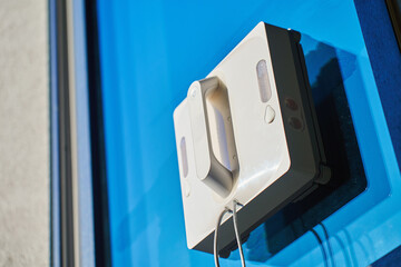 Square window cleaning robot washing glass. Robotic window cleaner working on window surface against blue sky. Smart home appliance concept