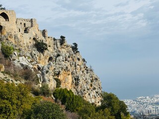 St. Hilarion Castle rising high in the Kyrenia Mountains with the distant coastal city of Kyrenia visible below, featuring dramatic cliffs, medieval stone walls, and sweeping views of northern Cyprus