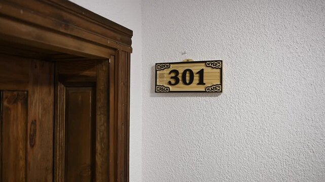 Stylish wooden carved hotel room sign on wall next to front door. Room number 301, sign for hotel, hostel, or residential complex. Elegant wooden door sign. Hotel business concept
