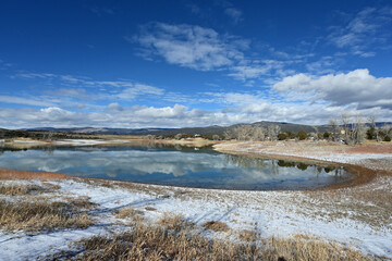 Obraz premium Sunny winter morning cloudscape over Grass Valley Reservoir in Harvey Gap State Park, Colorado reflected in reservoir's calm water.