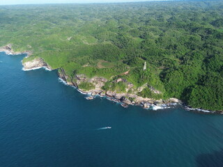 A dramatic view of the Gunung Sewu Geopark, featuring a coastal bay with steep limestone cliffs, turquoise waters, and rolling karst hills stretching across the horizon.