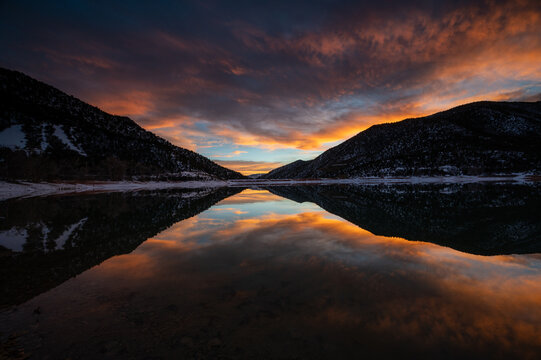 Intensely colorful sunset cloudscape over Grass Valley Reservoir in Harvey Gap State Park, Colorado reflected in reservoir's calm water.