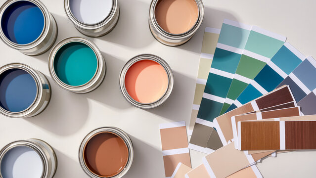 Paint cans with various colors (blues, greens, orange, brown, white) arranged on a white surface, with color swatch cards scattered nearby