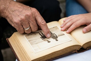 An elderly person points at an old photograph in a book while a child looks at it. They are in a calm setting, sharing a moment of connection through memories