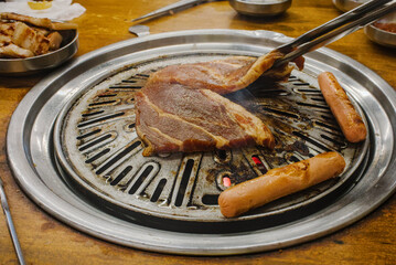 Close up of marinated pork and sausages cooking on an authentic Korean BBQ charcoal grill.