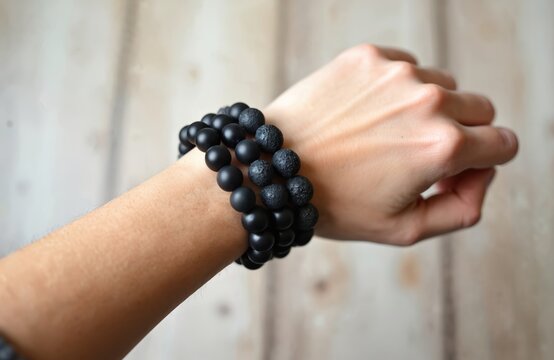 Three beaded bracelets, likely shungite and lava stone, adorn a person wrist against a textured wooden surface. The black matte beads and rougher stones create a striking contrast.