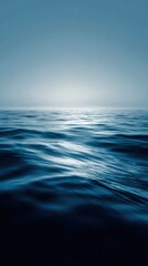 Waves roll gently under a clear sky at dawn near the ocean horizon, reflecting soft light from the early sun