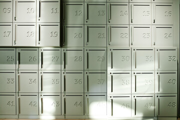 Numbered metal lockers arranged in grid pattern standing in bright indoor setting, sunlight casting geometric shadows across locker doors, emphasizing organized storage concept