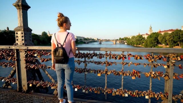 Woman standing on bridge with padlocks overlooking river in city