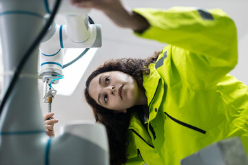 Female engineer closely inspecting and adjusting robotic arm components in high-tech industrial environment, symbolizing precision, innovation, smart automation.