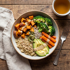 Delicious healthy buddha bowl featuring quinoa roasted sweet potatoes broccoli avocado carrots seeds and tahini dressing on rustic wood background