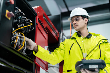 Engineer in safety uniform inspecting industrial control panel with cables in smart factory, representing maintenance, electrical systems, automation technology in modern manufacturing.