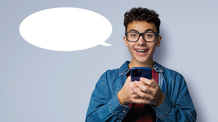 Expressive happy surprise curly hair man wear braces glasses eyeglasses hold cell phone cellular smartphone cellphone isolate grey gray background. White empty mockup speech bubble, free ad text space