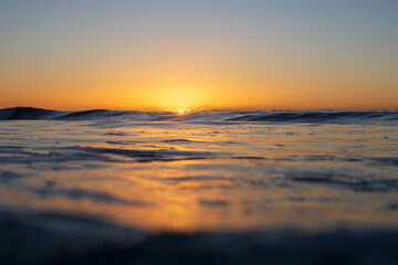 A warm golden sun rising over the oceans dark textured surface filling the sky with vibrant orange tones. Captured from a low perspective within the ocean on sunrise.